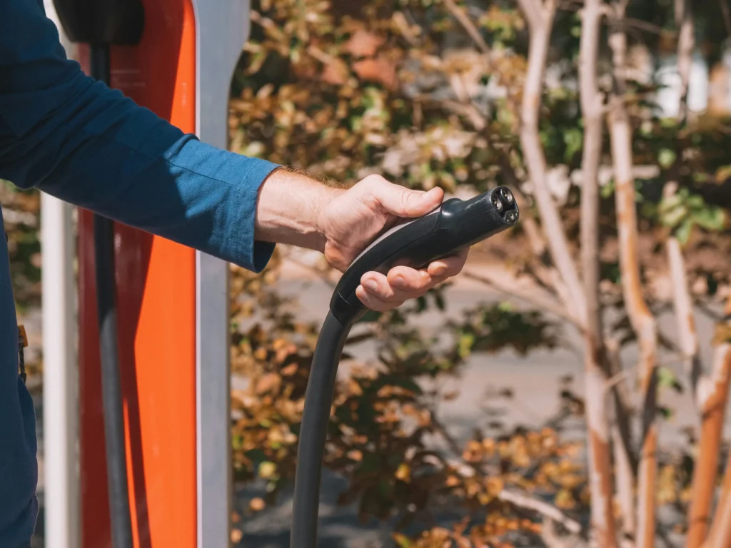 Person holding EV charger connector before plugging into electric vehicle charging port