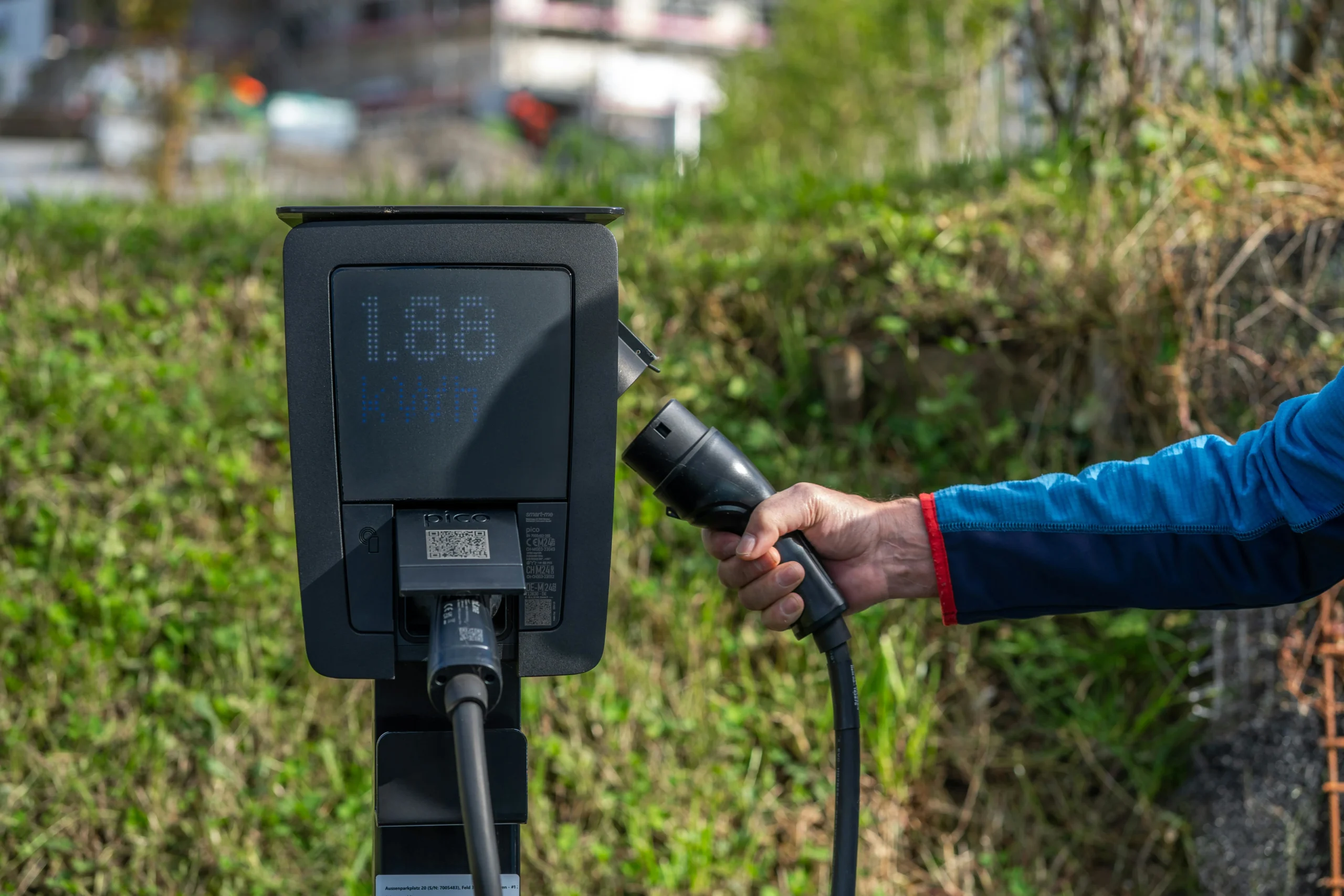 Person holding EV charger connector near a Level 2 charging station during electric vehicle charging setup
