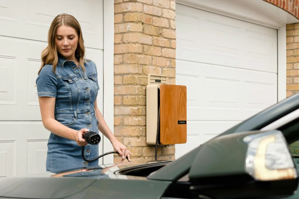 Woman using a Level 2 EV charger at home with a wall-mounted charging unit in a safe setup