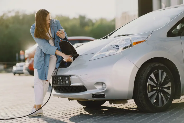 Woman plugging an electric vehicle into a public EV charging station