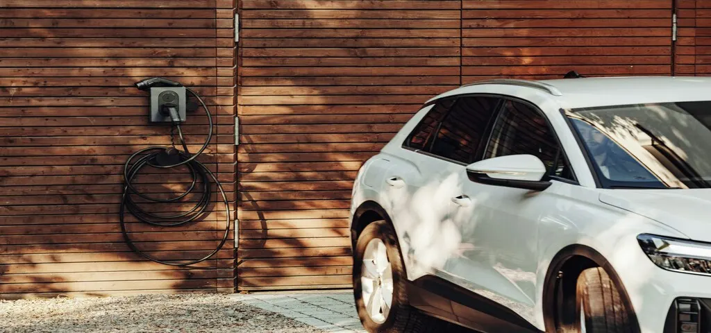 White electric car charging at a home EV charging station installed on an exterior wall